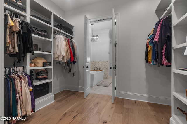 spacious closet featuring light hardwood / wood-style floors and a chandelier