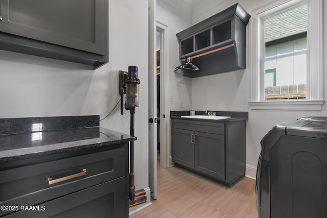 laundry room featuring washer and dryer, a sink, cabinet space, light wood-style floors, and baseboards