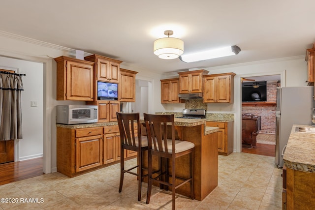 kitchen with a breakfast bar, brown cabinets, stainless steel appliances, crown molding, and light countertops