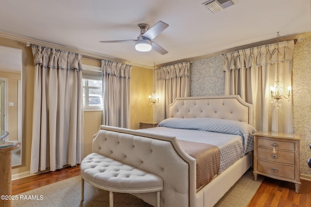 bedroom featuring visible vents, ornamental molding, a ceiling fan, wood finished floors, and wallpapered walls