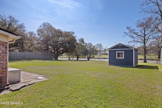 view of yard featuring an outbuilding, a storage shed, a water view, and fence