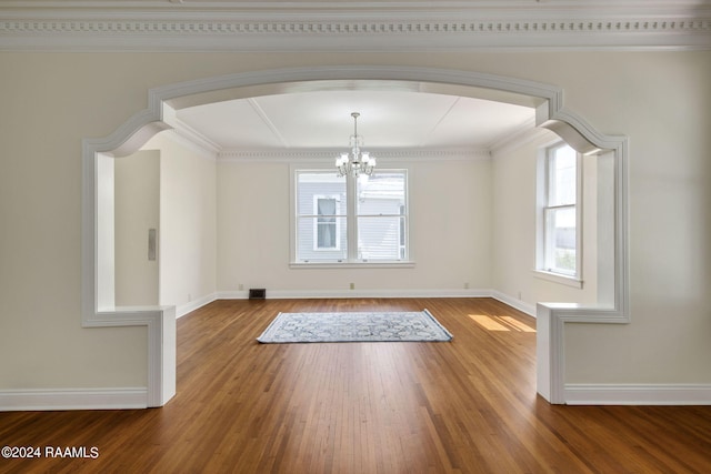 empty room featuring wood-type flooring, ornamental molding, and a chandelier