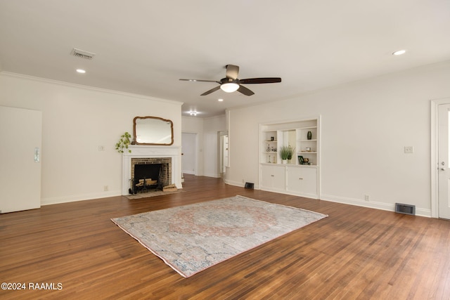 unfurnished living room featuring a fireplace, dark hardwood / wood-style flooring, ceiling fan, crown molding, and built in shelves