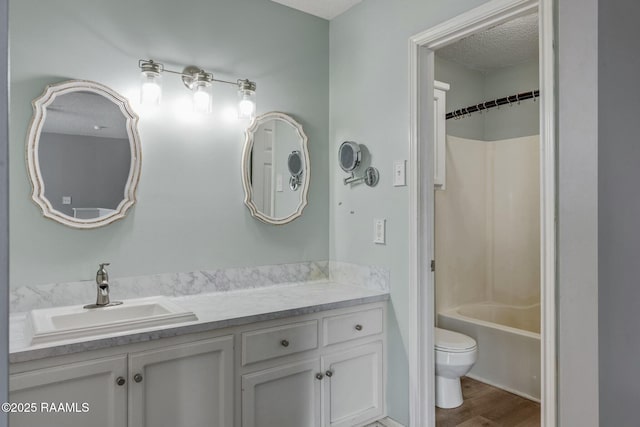 full bathroom with toilet, wood-type flooring, a textured ceiling, shower / bathing tub combination, and vanity