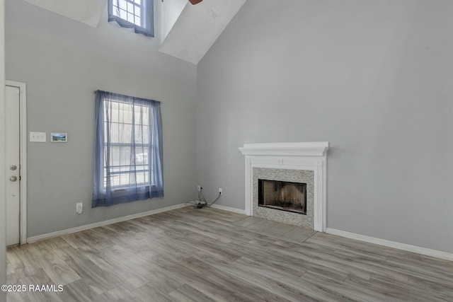 unfurnished living room with a towering ceiling, plenty of natural light, a tile fireplace, and light hardwood / wood-style floors