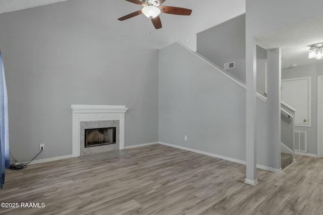 unfurnished living room featuring a textured ceiling, a high end fireplace, light hardwood / wood-style floors, and ceiling fan