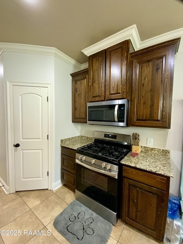 kitchen with light stone counters, dark brown cabinets, light tile patterned floors, ornamental molding, and appliances with stainless steel finishes