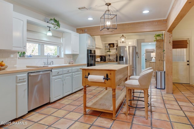 kitchen with white cabinetry, hanging light fixtures, ornamental molding, appliances with stainless steel finishes, and backsplash