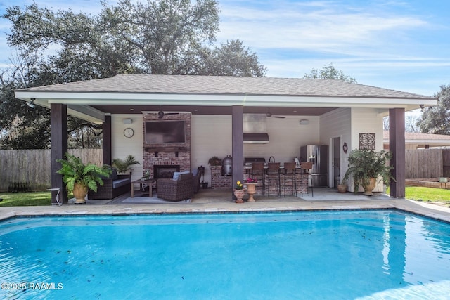 view of swimming pool with a patio area, exterior bar, ceiling fan, a grill, and an outdoor living space with a fireplace