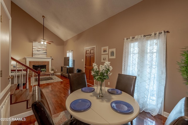 dining space featuring hardwood / wood-style floors, a fireplace, high vaulted ceiling, and ceiling fan