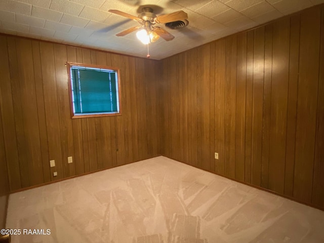 carpeted spare room with ceiling fan and wood walls