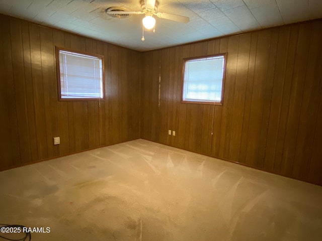 carpeted empty room with ceiling fan and wood walls