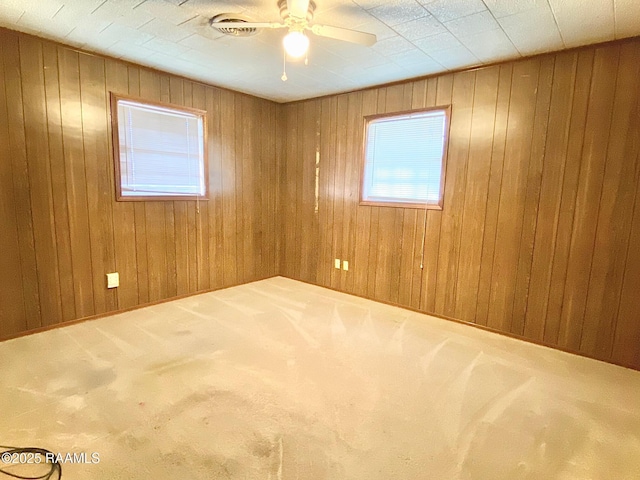 carpeted spare room with wood walls and a ceiling fan