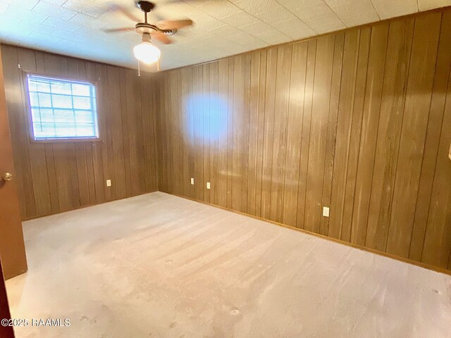 carpeted spare room featuring wood walls and ceiling fan