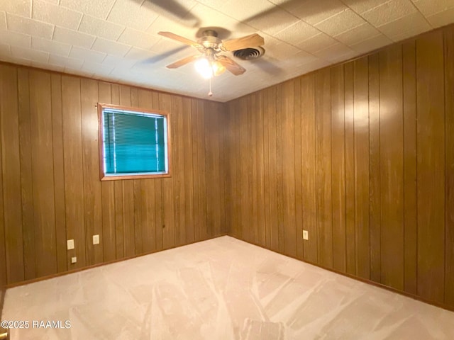 empty room featuring wood walls, a ceiling fan, and carpet floors