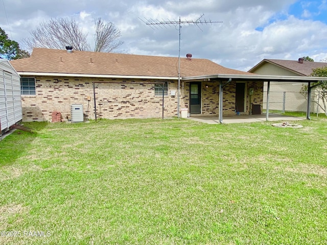 back of property featuring a lawn, a shingled roof, brick siding, and a patio area