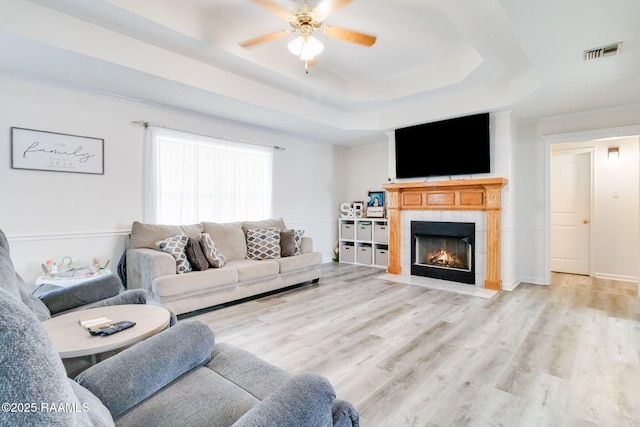 living room with crown molding, light hardwood / wood-style flooring, a raised ceiling, ceiling fan, and a fireplace