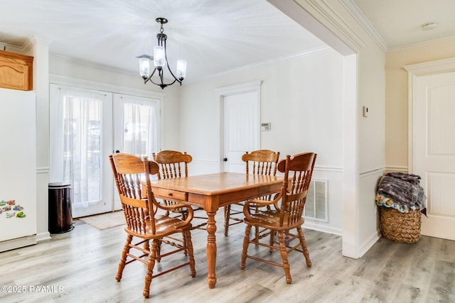 dining area featuring french doors, ornamental molding, an inviting chandelier, and light hardwood / wood-style flooring