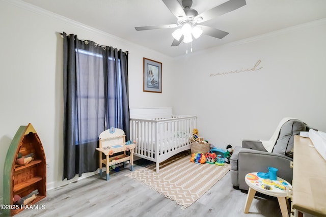 bedroom featuring crown molding, ceiling fan, a nursery area, and light wood-type flooring