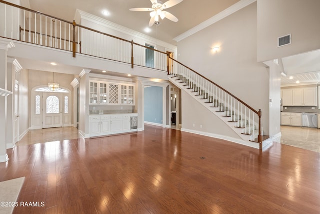 unfurnished living room with bar, light hardwood / wood-style flooring, ornamental molding, ceiling fan, and a high ceiling