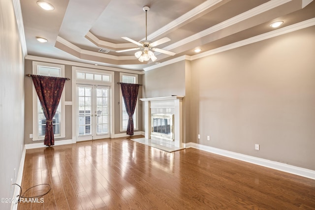 unfurnished living room with a raised ceiling, a premium fireplace, hardwood / wood-style flooring, and french doors