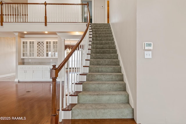 stairway featuring indoor bar, wood-type flooring, ornamental molding, and a towering ceiling