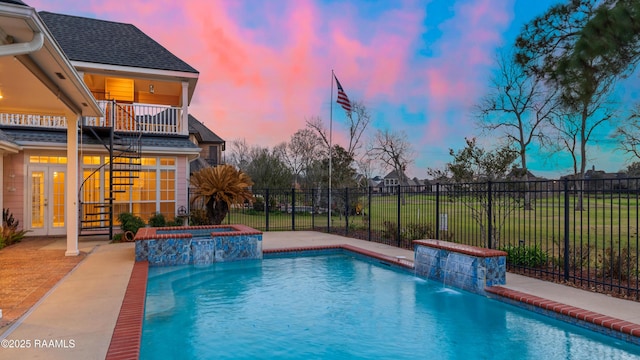 pool at dusk featuring a patio, french doors, pool water feature, and an in ground hot tub