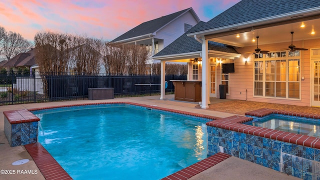 pool at dusk with an in ground hot tub, pool water feature, ceiling fan, and a patio