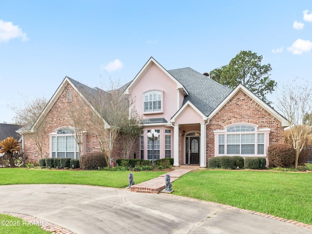 view of front of property featuring a shingled roof, stucco siding, brick siding, and a front lawn