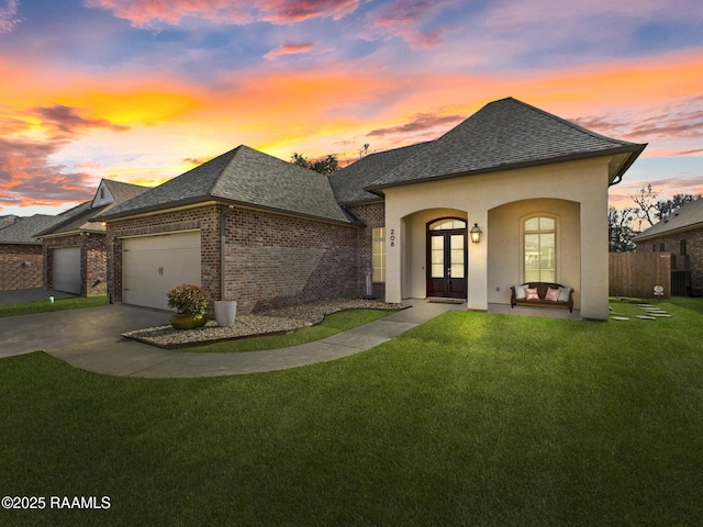 french country home with a shingled roof, french doors, brick siding, and a front lawn