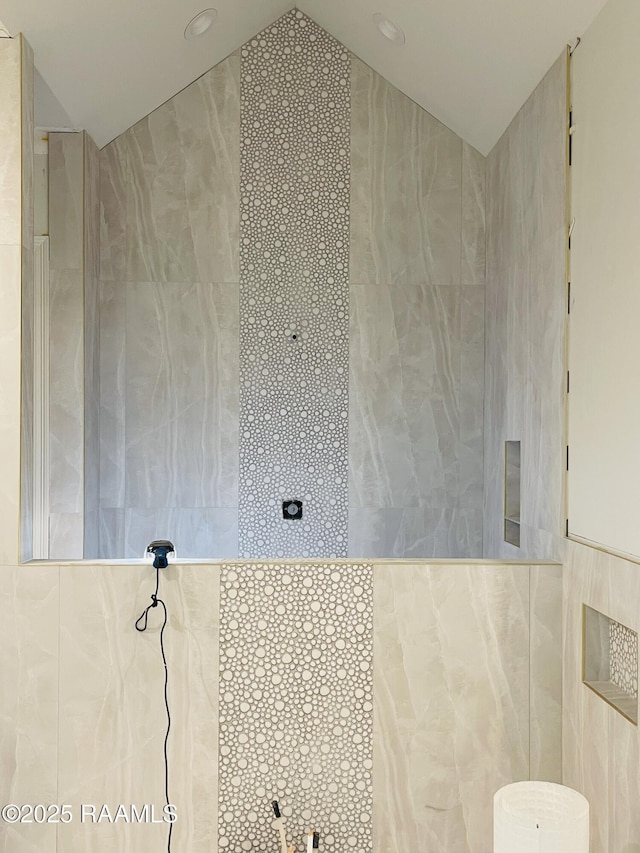 bathroom featuring tile walls, vaulted ceiling, and a tile shower