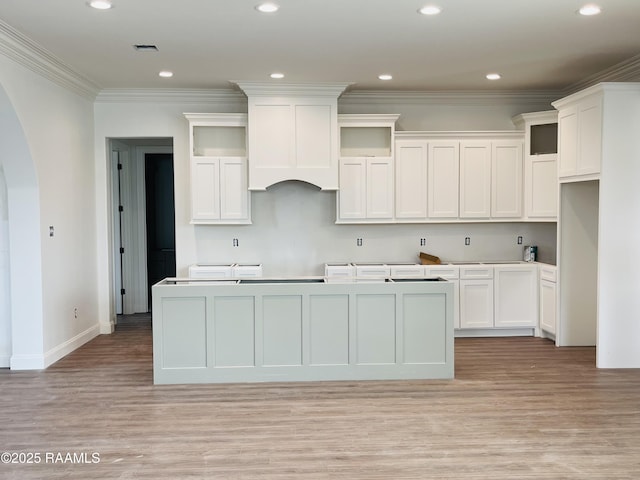 kitchen featuring a center island with sink, ornamental molding, custom range hood, light hardwood / wood-style floors, and white cabinets