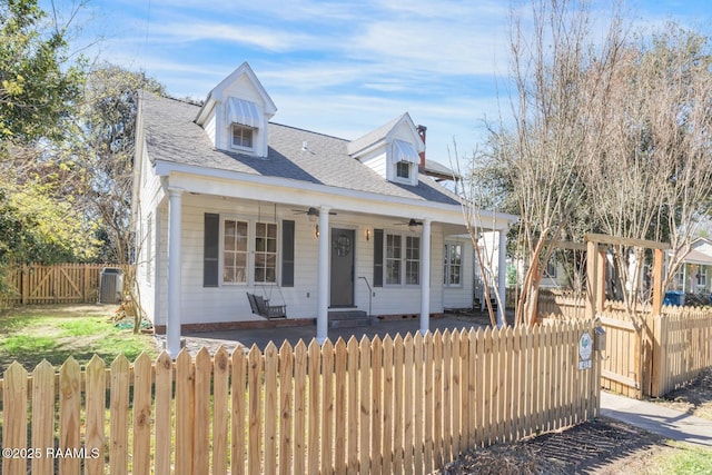 cape cod home with a porch, a shingled roof, a fenced front yard, and a ceiling fan