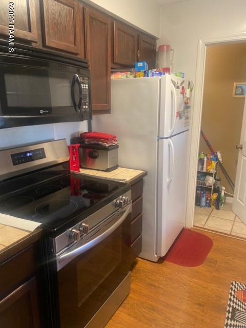 kitchen with electric stove, light hardwood / wood-style flooring, white refrigerator, dark brown cabinetry, and tile counters