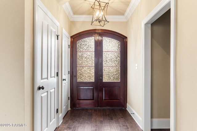 entrance foyer with an inviting chandelier, dark wood-type flooring, ornamental molding, and french doors