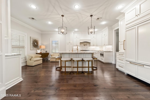 kitchen with a breakfast bar, a kitchen island with sink, ornamental molding, white cabinets, and decorative light fixtures