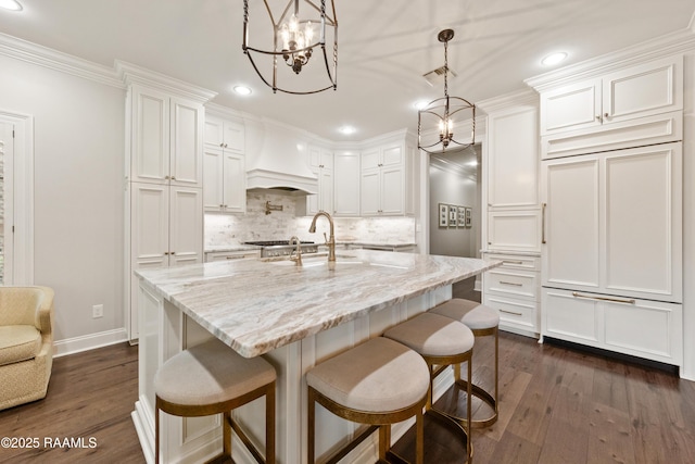 kitchen with pendant lighting, white cabinetry, light stone countertops, and wall chimney exhaust hood