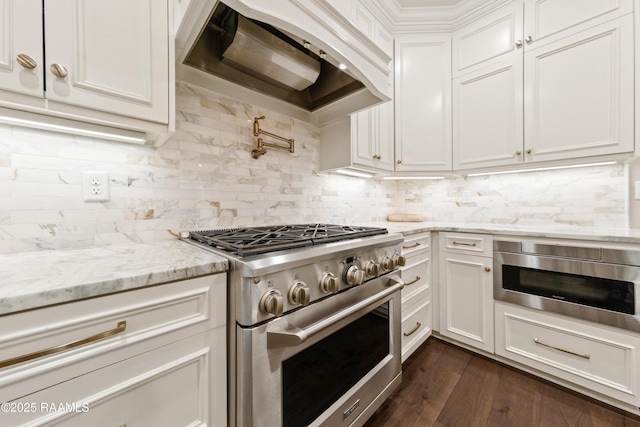 kitchen featuring tasteful backsplash, white cabinetry, light stone counters, stainless steel appliances, and custom range hood