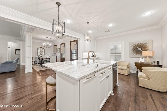 kitchen featuring sink, decorative columns, light stone counters, an island with sink, and white cabinets