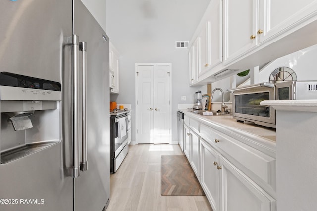 kitchen featuring white cabinetry, stainless steel appliances, sink, and light hardwood / wood-style flooring