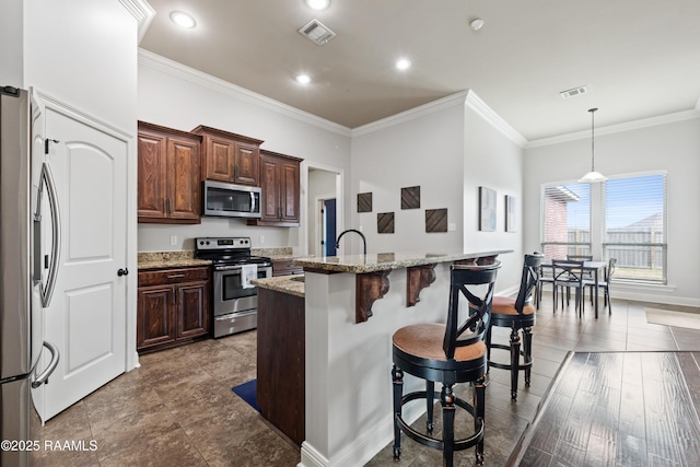 kitchen featuring a kitchen bar, stainless steel appliances, light stone counters, a center island with sink, and decorative light fixtures