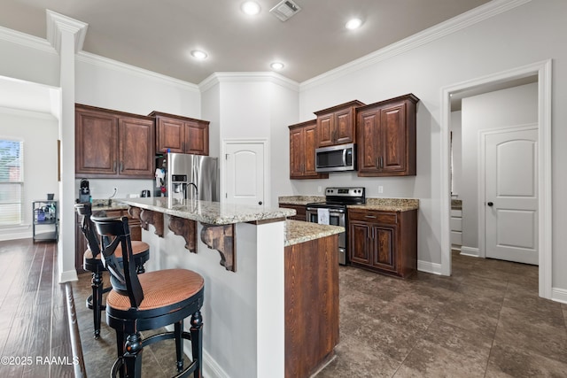 kitchen featuring appliances with stainless steel finishes, a breakfast bar, crown molding, light stone countertops, and a center island with sink