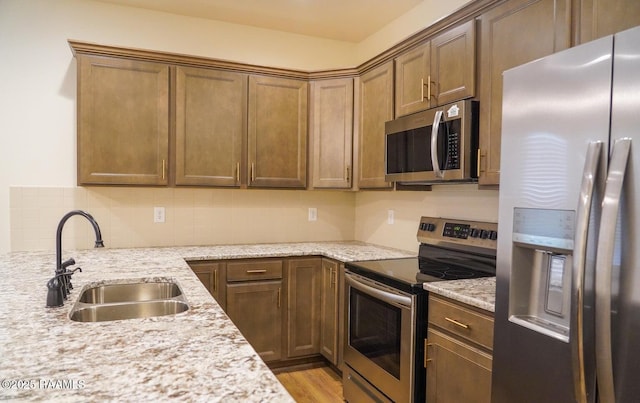 kitchen with sink, appliances with stainless steel finishes, light stone counters, decorative backsplash, and light wood-type flooring