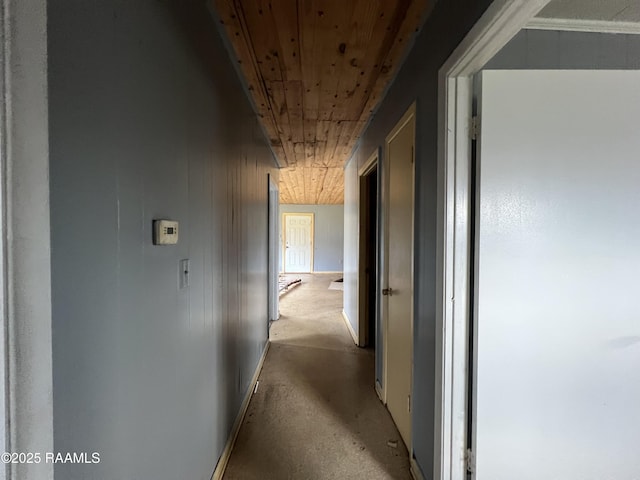 hallway featuring wood ceiling, concrete floors, wooden walls, and baseboards