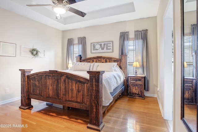 bedroom with multiple windows, a tray ceiling, and light wood-type flooring