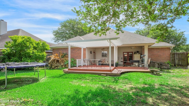 back of property featuring brick siding, fence, a trampoline, and a deck