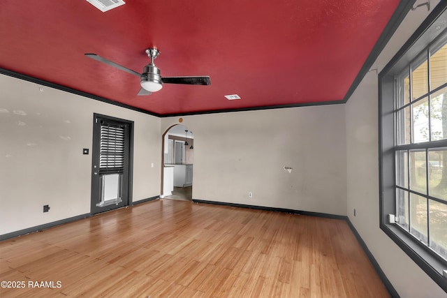 unfurnished room featuring crown molding, baseboards, arched walkways, a ceiling fan, and wood finished floors