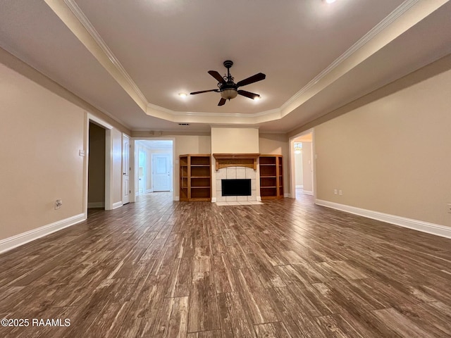 unfurnished living room with crown molding, ceiling fan, a tray ceiling, a fireplace, and dark hardwood / wood-style flooring