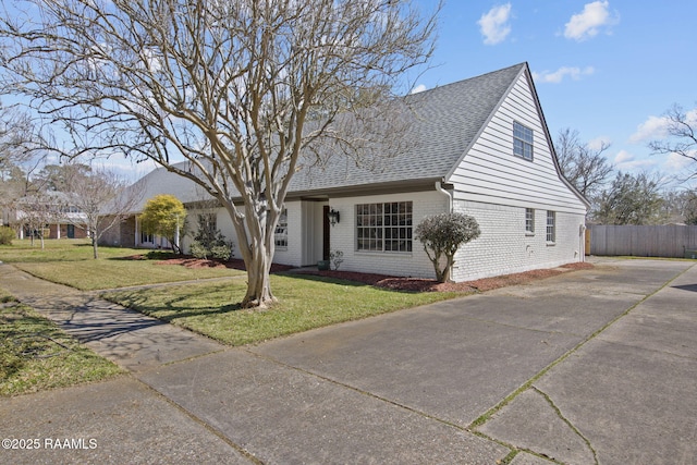 view of front facade featuring a front lawn, roof with shingles, fence, and brick siding