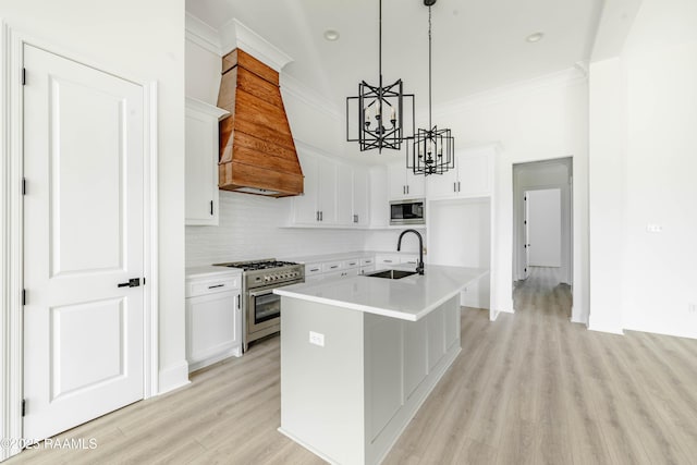 kitchen featuring built in microwave, sink, an island with sink, high end stove, and white cabinets